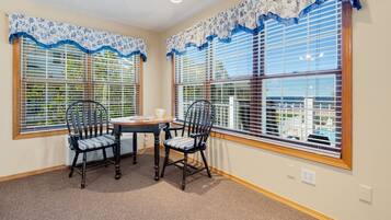 A room with two large windows, a table with chairs, and a view of a residential area.