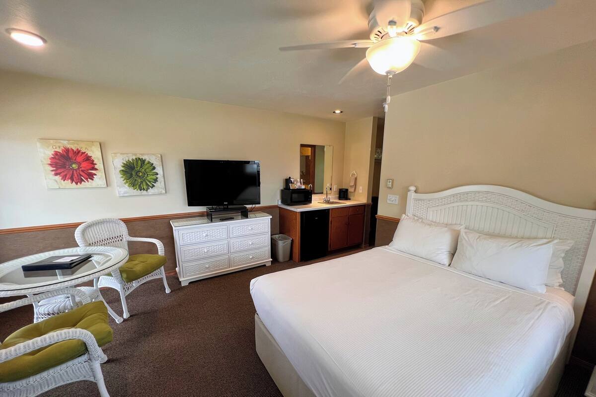 A hotel room with a bed, a desk with a flat-screen TV, a white dresser, and two chairs.