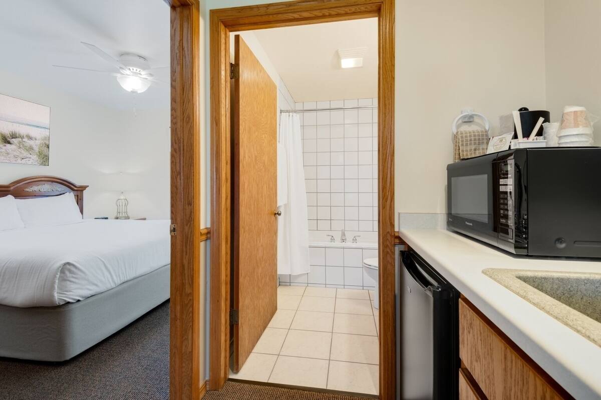 A hotel room with a bed, a bathroom with a shower, and a kitchenette with a microwave.