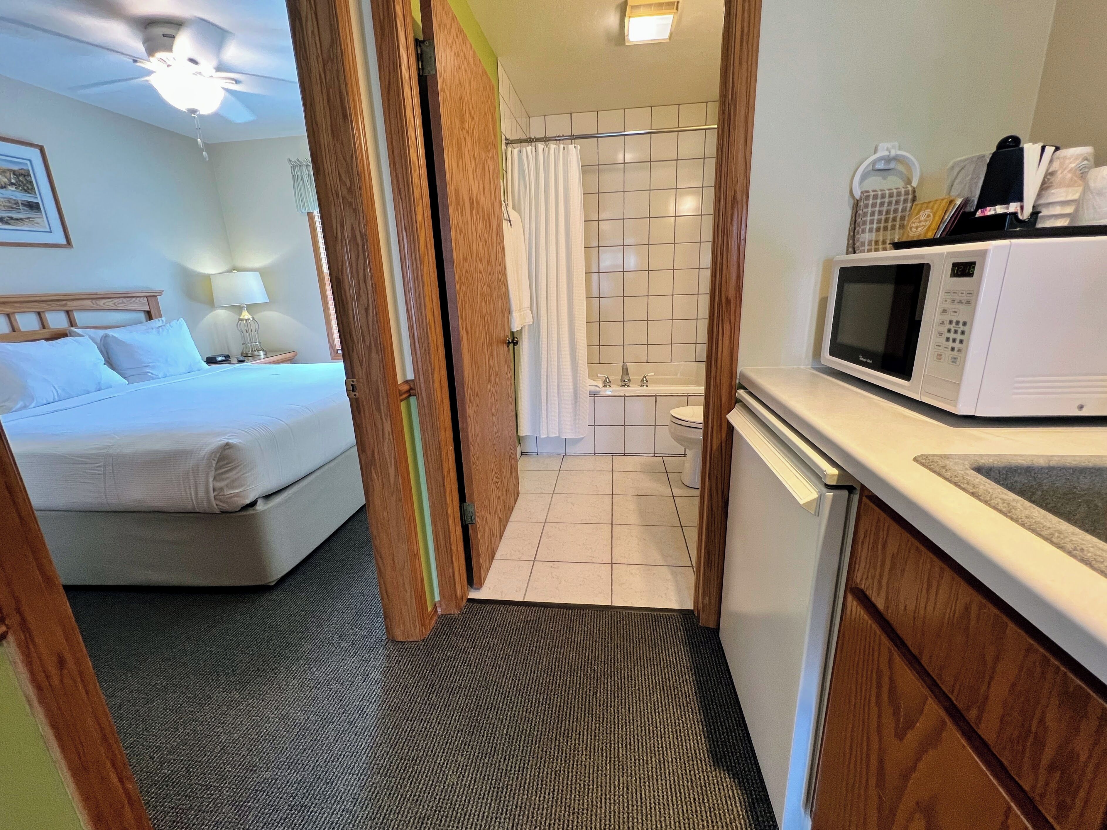 A hotel room with a bed, a bathroom with a shower, a microwave, and a sink.