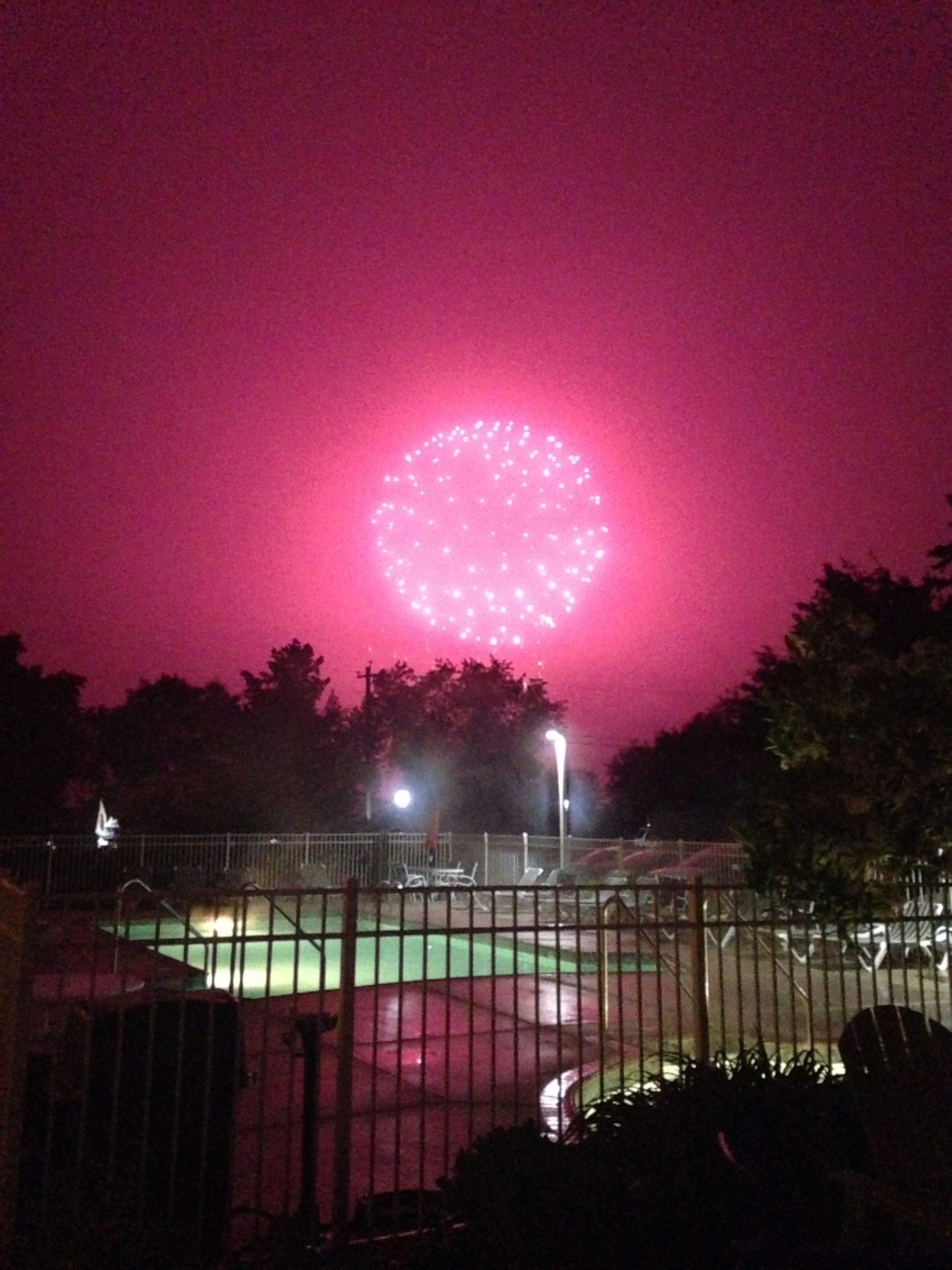 A nighttime view of a fenced area with a circular light display in the sky.