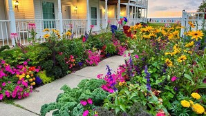 A two-story building with a porch, surrounded by a variety of colorful flowers and plants. - Bay Breeze Resort (Ephraim)
