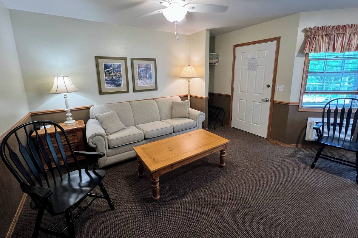 A living room with a sofa, two chairs, a coffee table, a ceiling fan, and framed pictures on the wall.