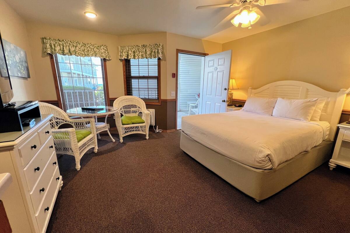 A bedroom with a bed, a desk, two chairs, a dresser, and a ceiling fan.