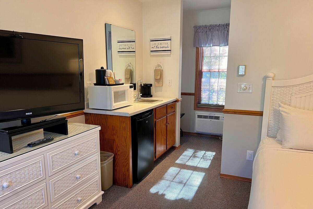 A compact hotel room with a television, kitchenette, and a bed.