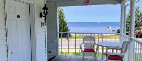 A porch with a white door, two wicker chairs with red cushions, and a view of the ocean.