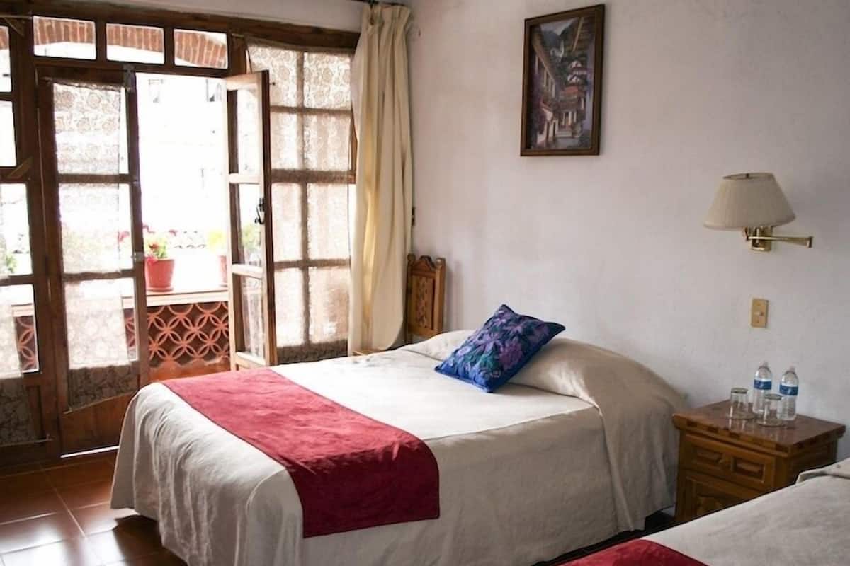 Une chambre avec deux lits, une fenêtre donnant sur un beau paysage, un tableau au mur et une table de chevet avec des bouteilles d’eau.