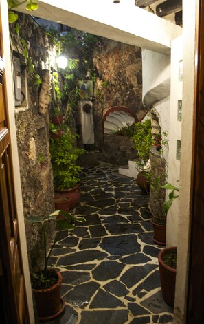 A narrow stone pathway leading through a rustic building with potted plants and a stone wall.