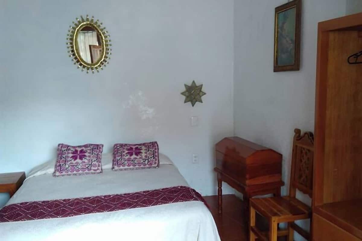 Une chambre à coucher avec un lit, une chaise en bois, une petite table et une armoire.