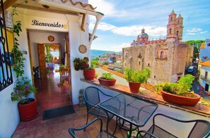 A balcony with potted plants, a table, and chairs, overlooking a historic building with a clock tower. - Hotel Mi Casita (Taxco)