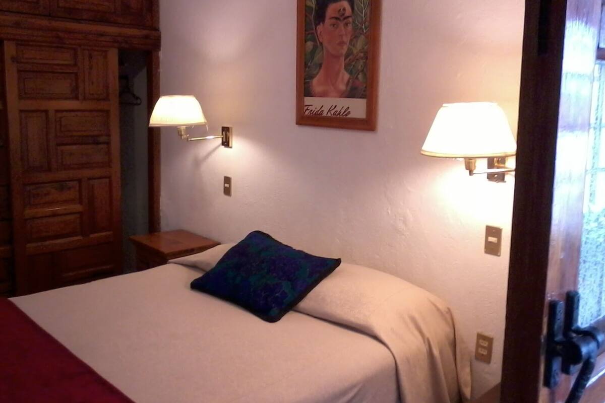 Une chambre d’hôtel avec un lit, deux lampes fixées au mur, une armoire en bois et un tableau encadré accroché au mur.