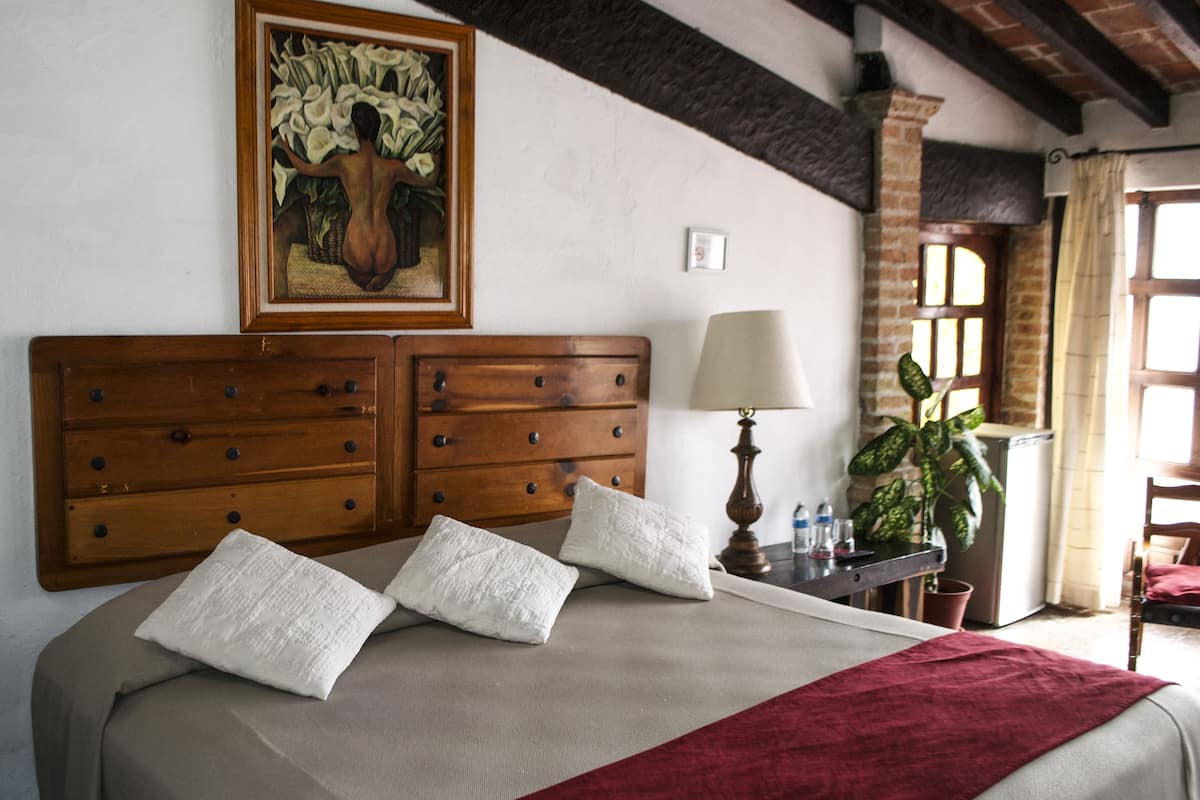 Une chambre d’hôtel avec un grand lit, une tête de lit en bois, un tableau au-dessus du lit, une lampe et une plante en pot.