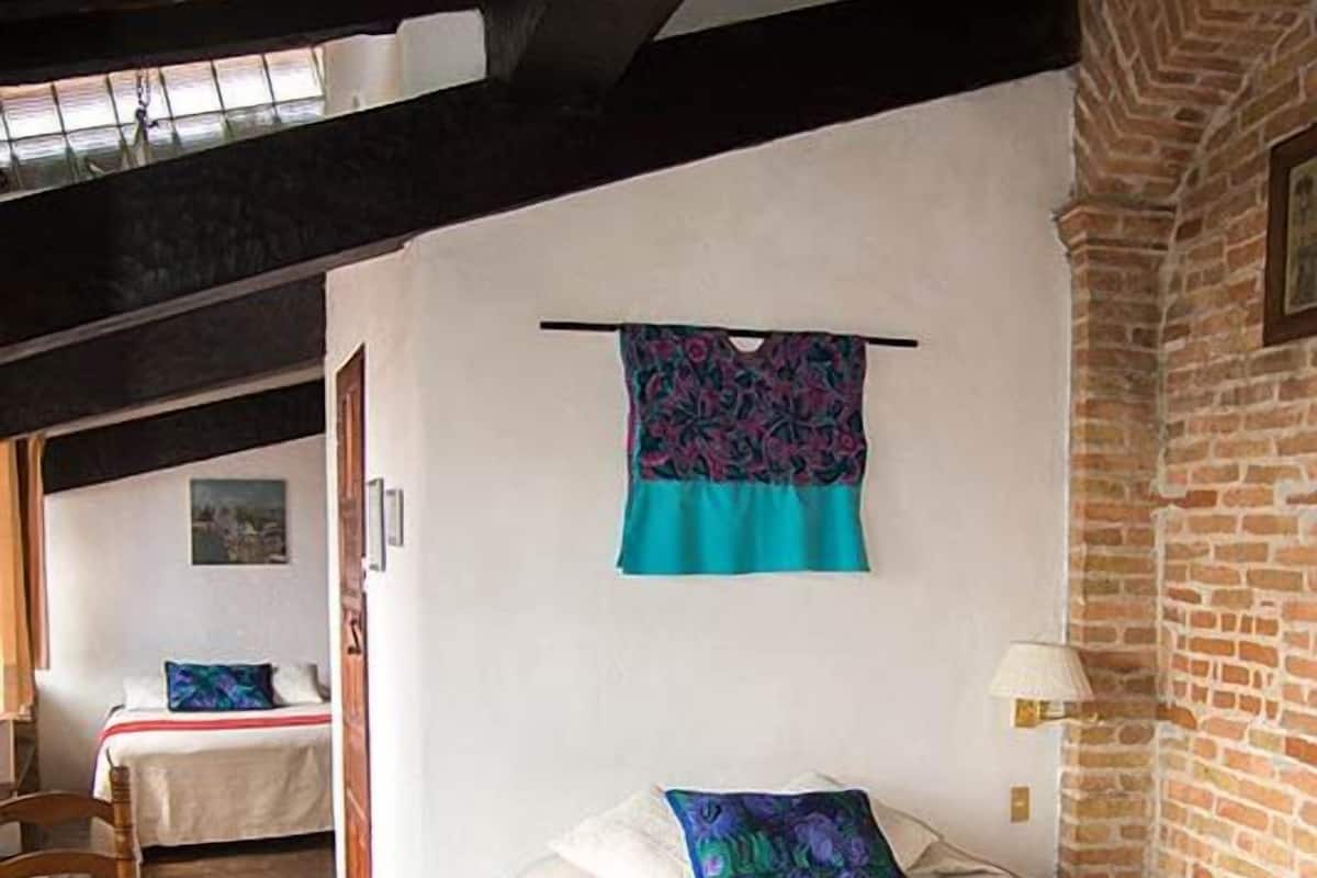 Une pièce avec un lit, une chaise, une table et un mur en briques.