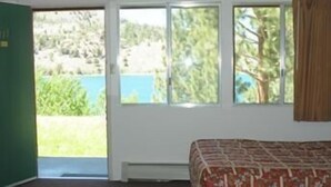 A bedroom with a bed, a window with a view of greenery and a body of water, and a door.