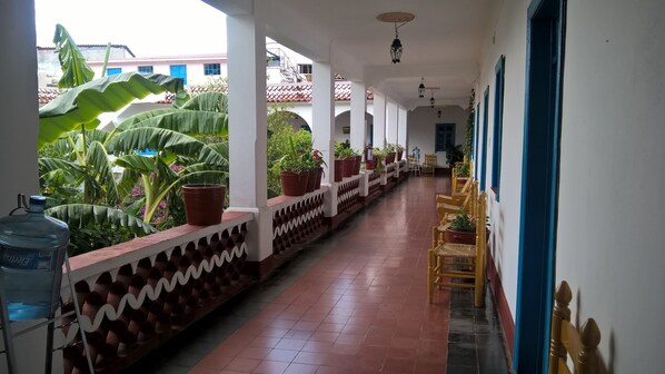 A covered corridor with potted plants, a water dispenser, and yellow chairs. - Hotel Santa Prisca (Taxco)