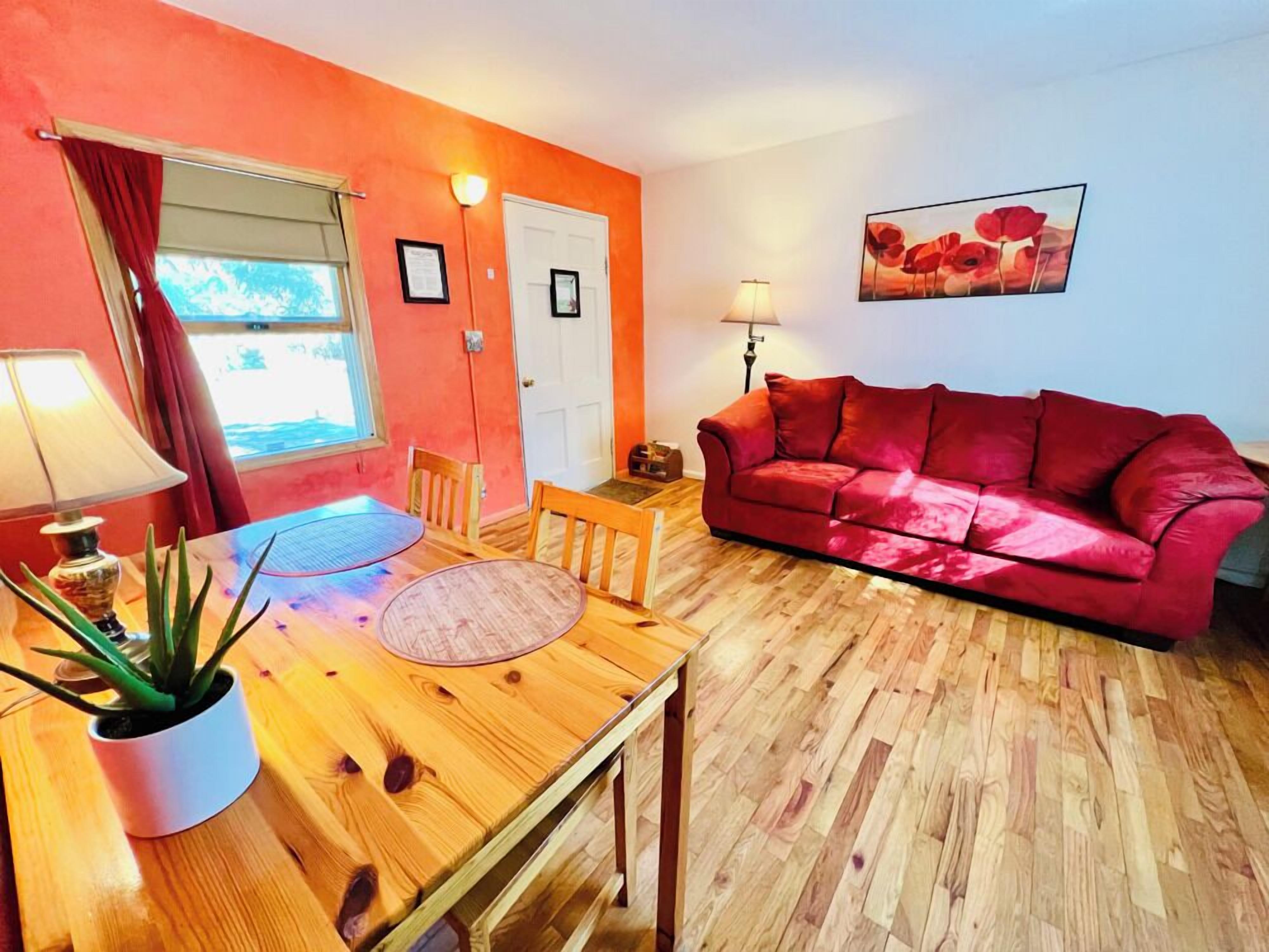 A cozy living room with a red sofa, wooden dining table, and a potted plant.