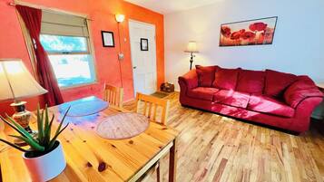A cozy living room with a red sofa, wooden dining table, and a potted plant.