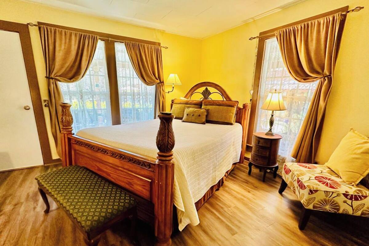 Un dormitorio ordenado con una cama de madera, un banco, una silla y una mesita de noche con una lámpara.