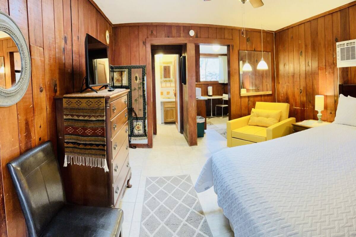 Una habitación con paneles de madera, una cama grande, una silla, un tocador y un espejo.