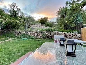 Un patio con muro de piedra, zona verde y atardecer de fondo.