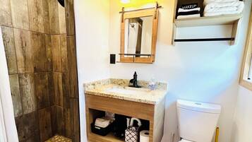 A bathroom with a wooden shower enclosure, a sink with a vanity, a toilet, and a shelf with towels.