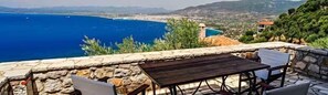 A stone patio with a table and chairs overlooking a coastal view. - Diotima's Homes (Kalamata)
