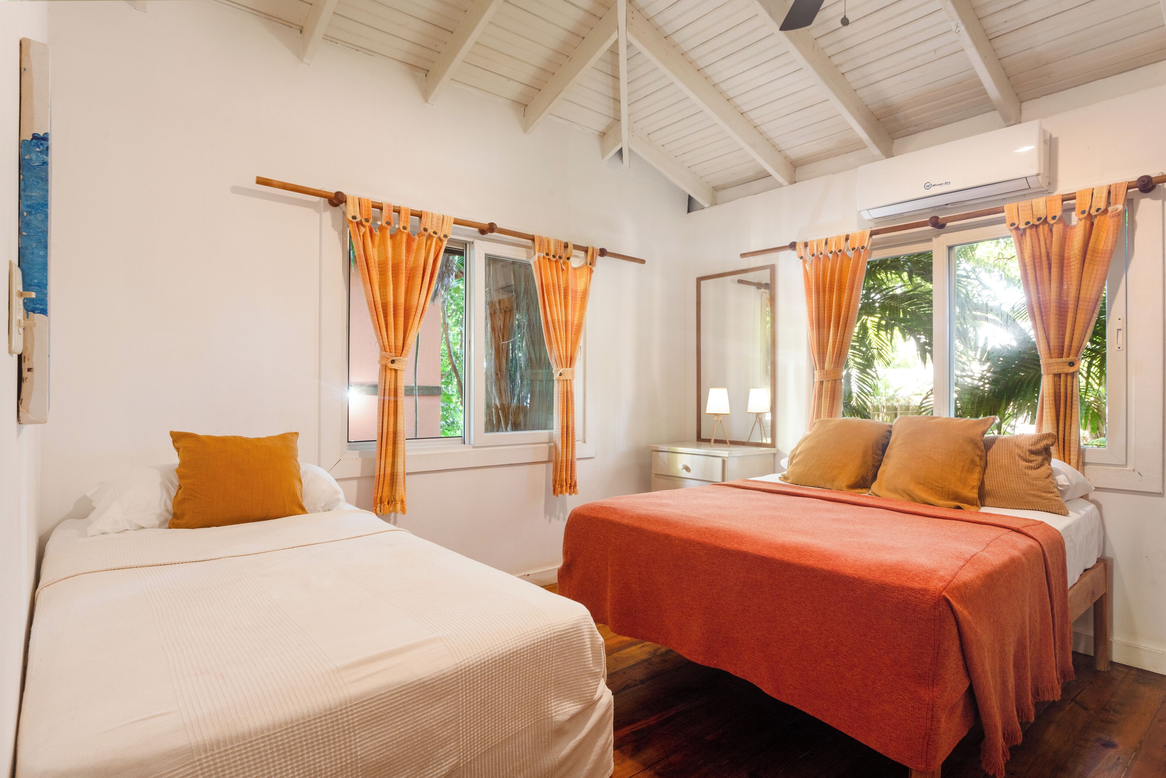 A room with two beds, a window with curtains, a bedside table, and a mirror.