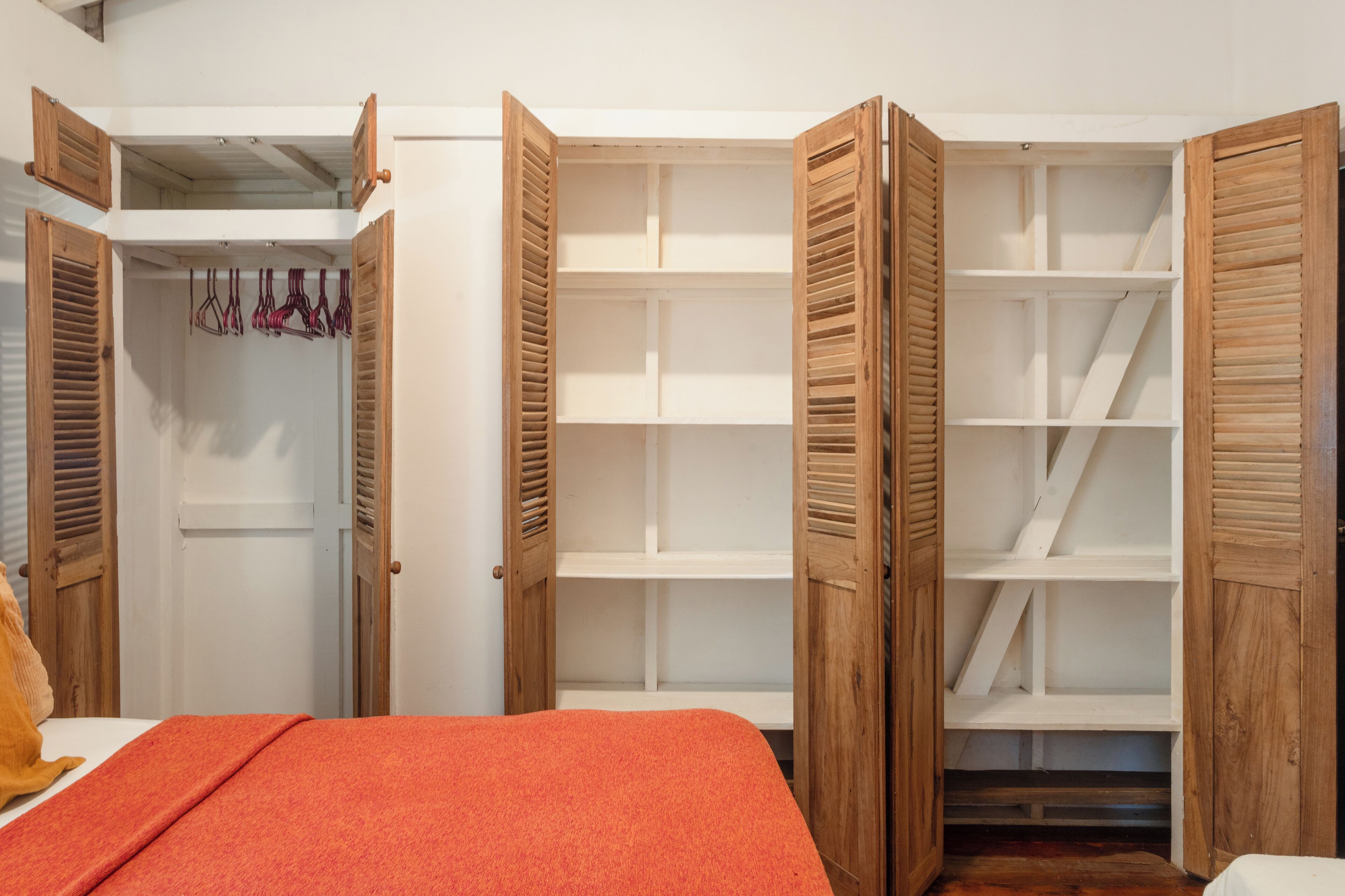 Een slaapkamer met een bed, een open kast met meerdere planken en een kledingrek met kleding.