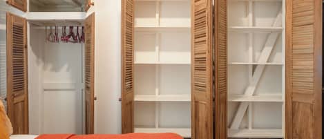 Een slaapkamer met een bed, een open kast met meerdere planken en een kledingrek met kleding.