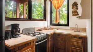 A kitchen with a gas stove, a coffee maker, a sink, and wooden cabinets. - Posada Arco Iris (Roatan)