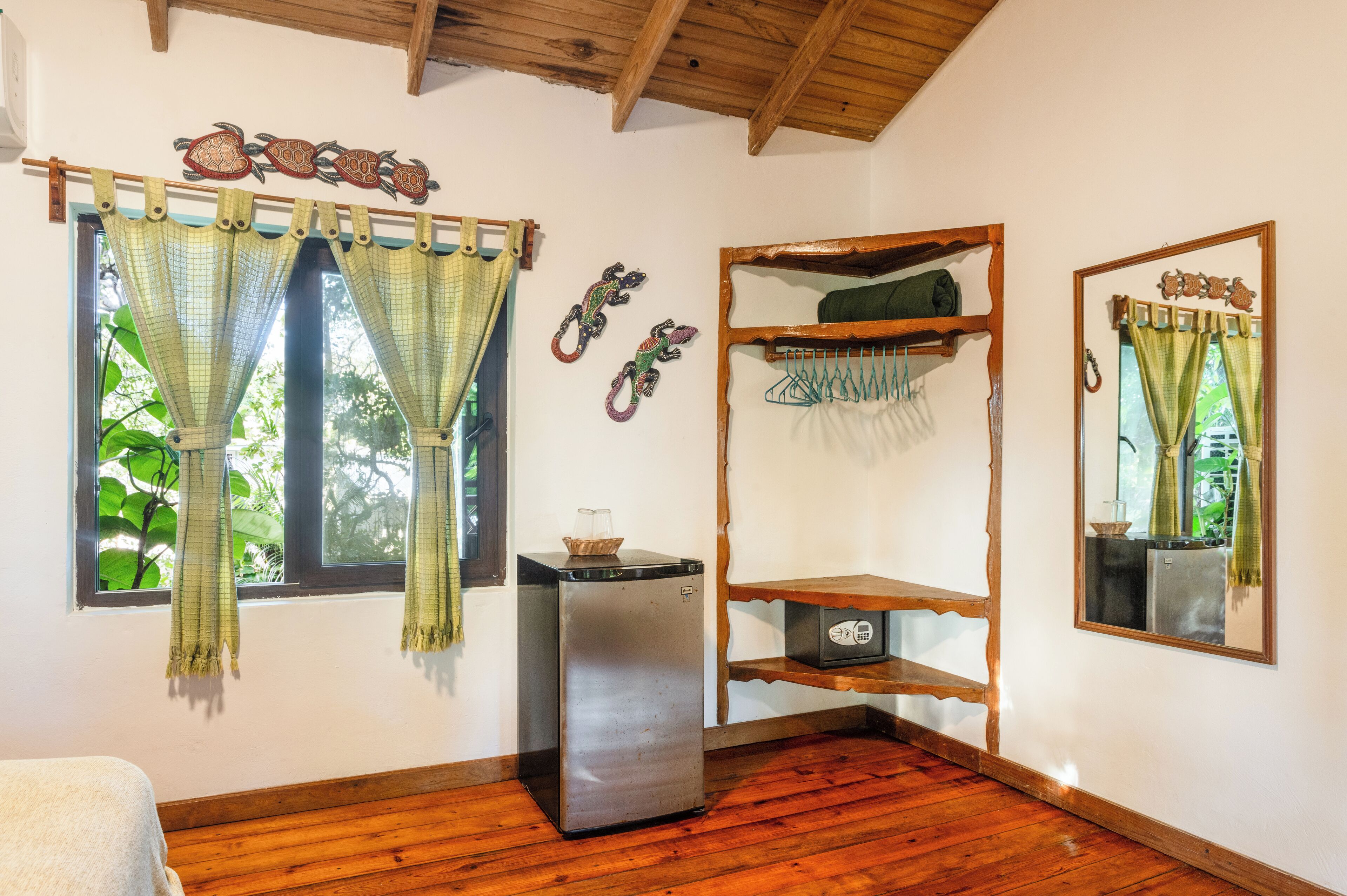 A compact kitchen with a refrigerator, wooden shelves, and a window with curtains.