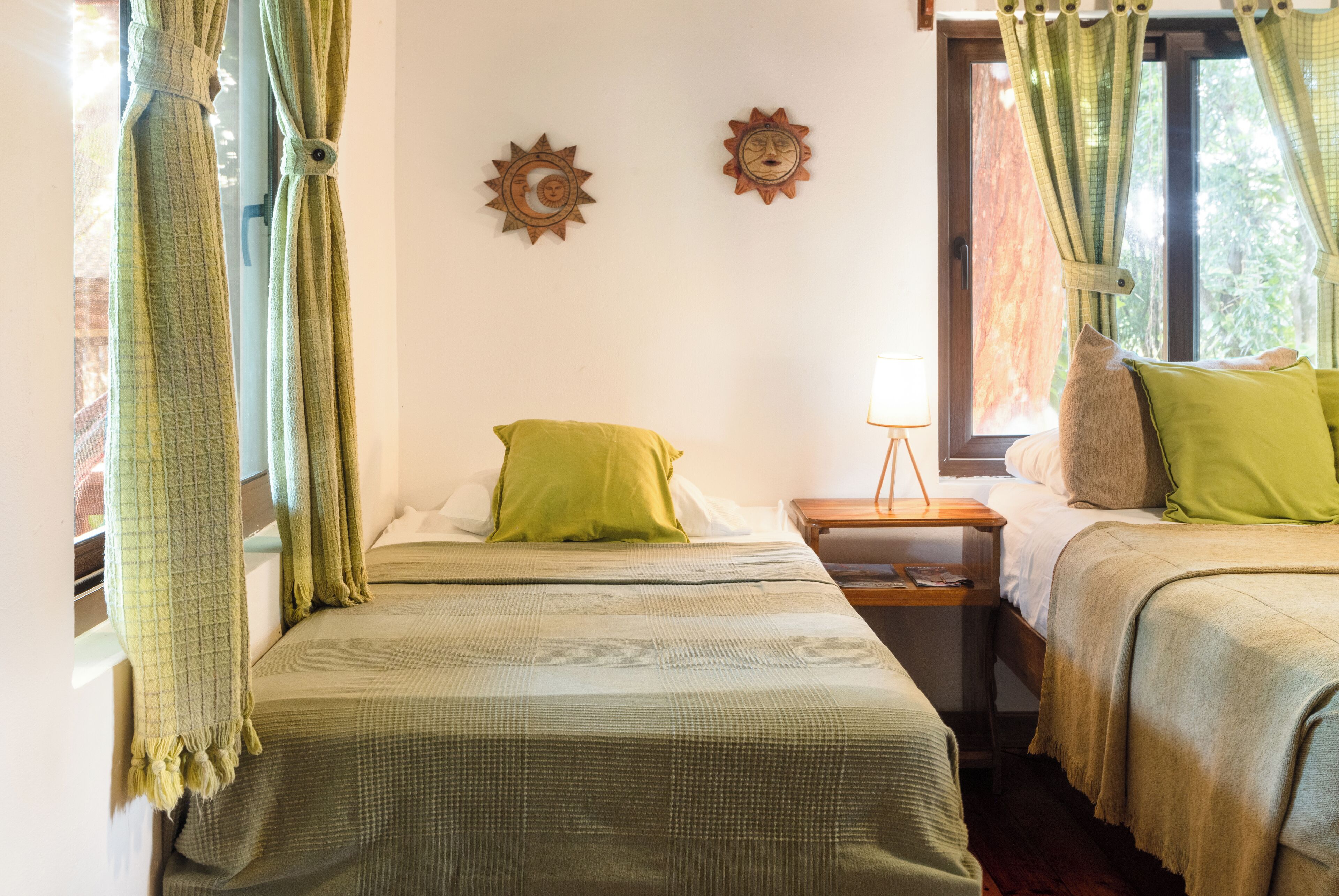 Una habitación con dos camas, una mesita de noche con lámpara y una ventana con cortinas.