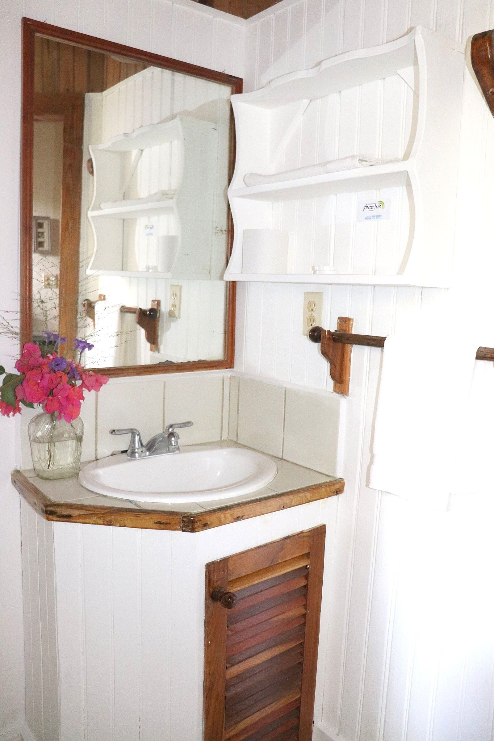 A bathroom with a wooden vanity, a white sink, and a mirror with a wooden frame.