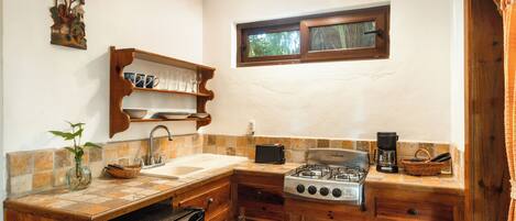 Una cocina pequeña con estufa a gas, pileta y alacenas de madera.
