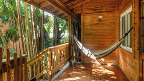 A wooden cabin with a hammock, wooden deck, and a view of palm trees. - Posada Arco Iris (Roatan)