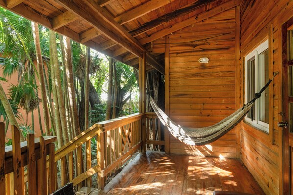 A wooden cabin with a hammock, wooden deck, and a view of palm trees.