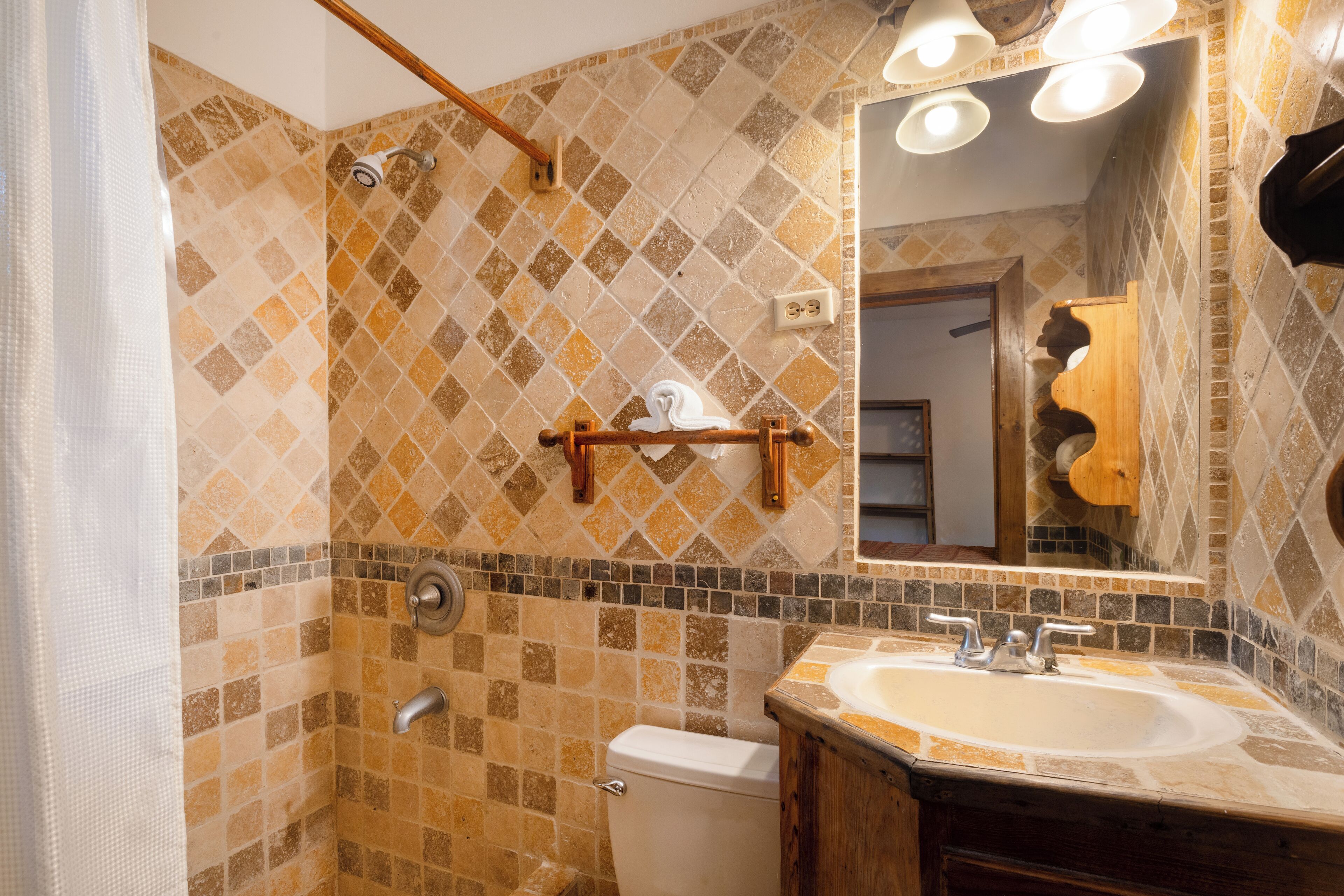 Een badkamer met betegelde douchewand, toilet, wastafel met spiegel en handdoekrek.
