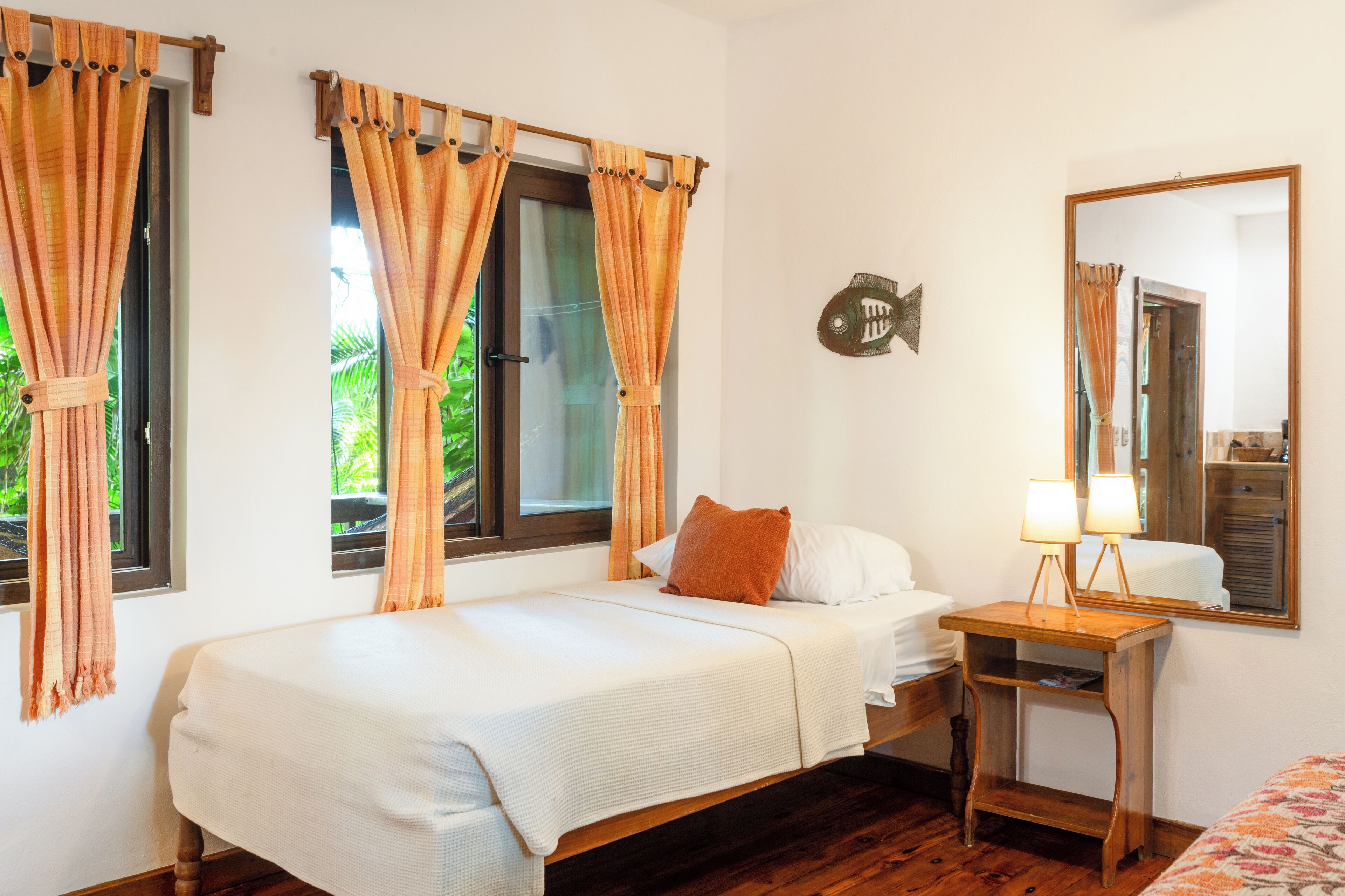 A bedroom with a single bed, a wooden nightstand, a mirror, and curtains on the windows.