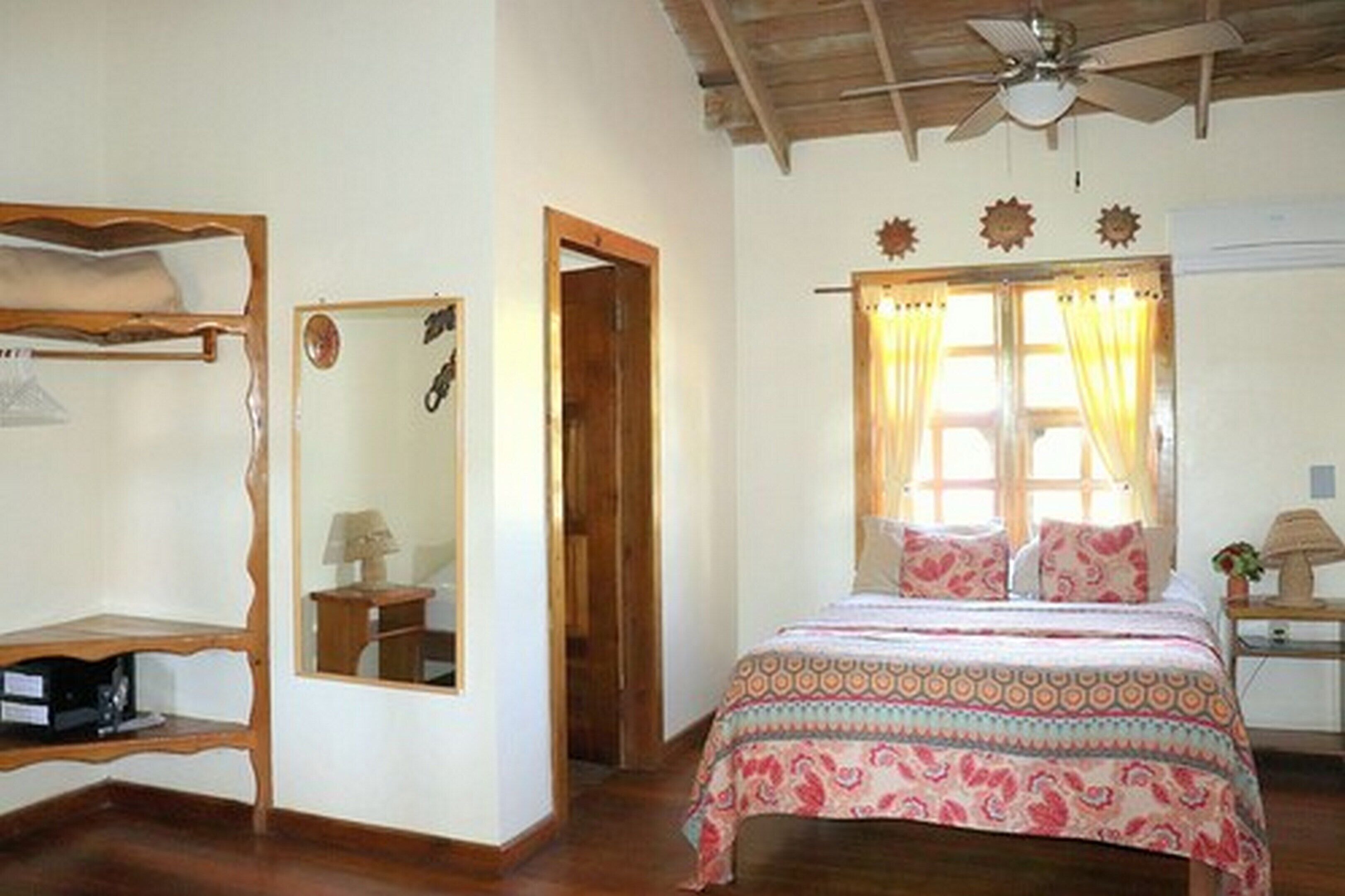 A bedroom with a bed, a ceiling fan, a window with curtains, and a door.
