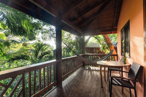 A wooden deck with a hammock, a table, and chairs overlooking lush greenery. - Posada Arco Iris (Roatan)