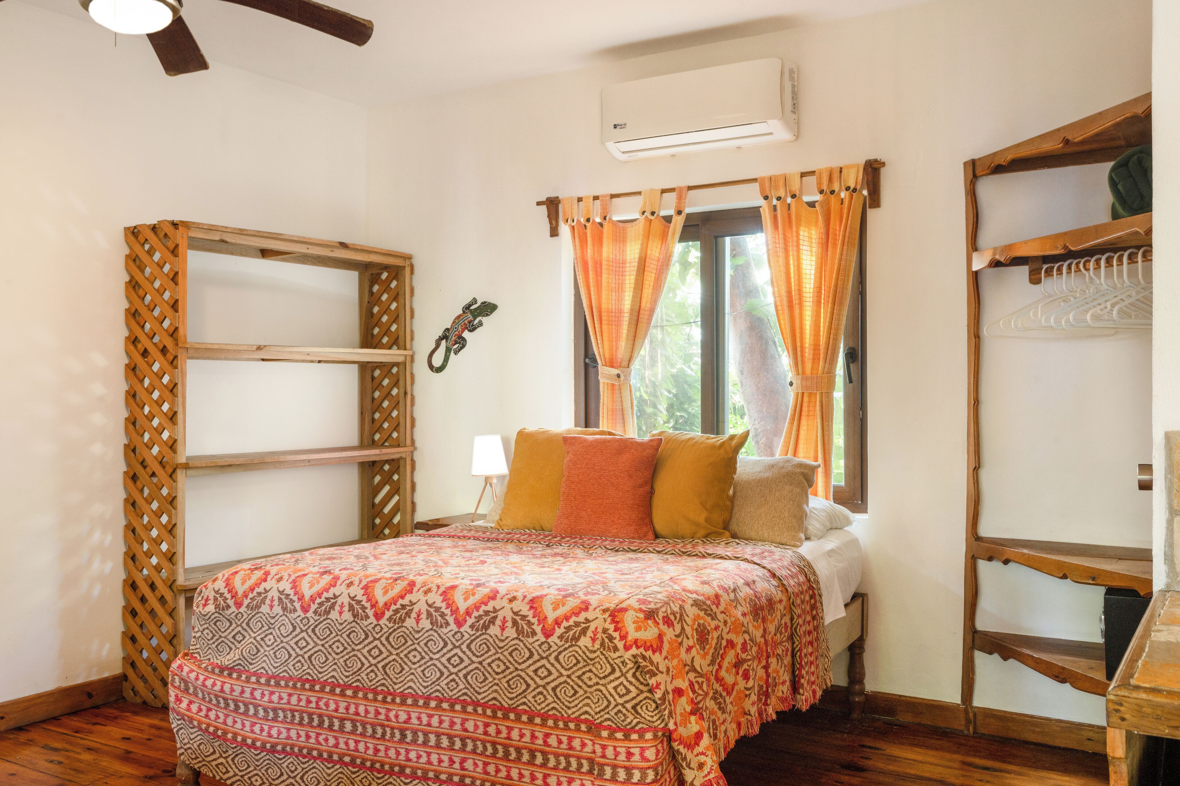 A bedroom with a bed, a wooden wardrobe, a window with curtains, and a ceiling fan.