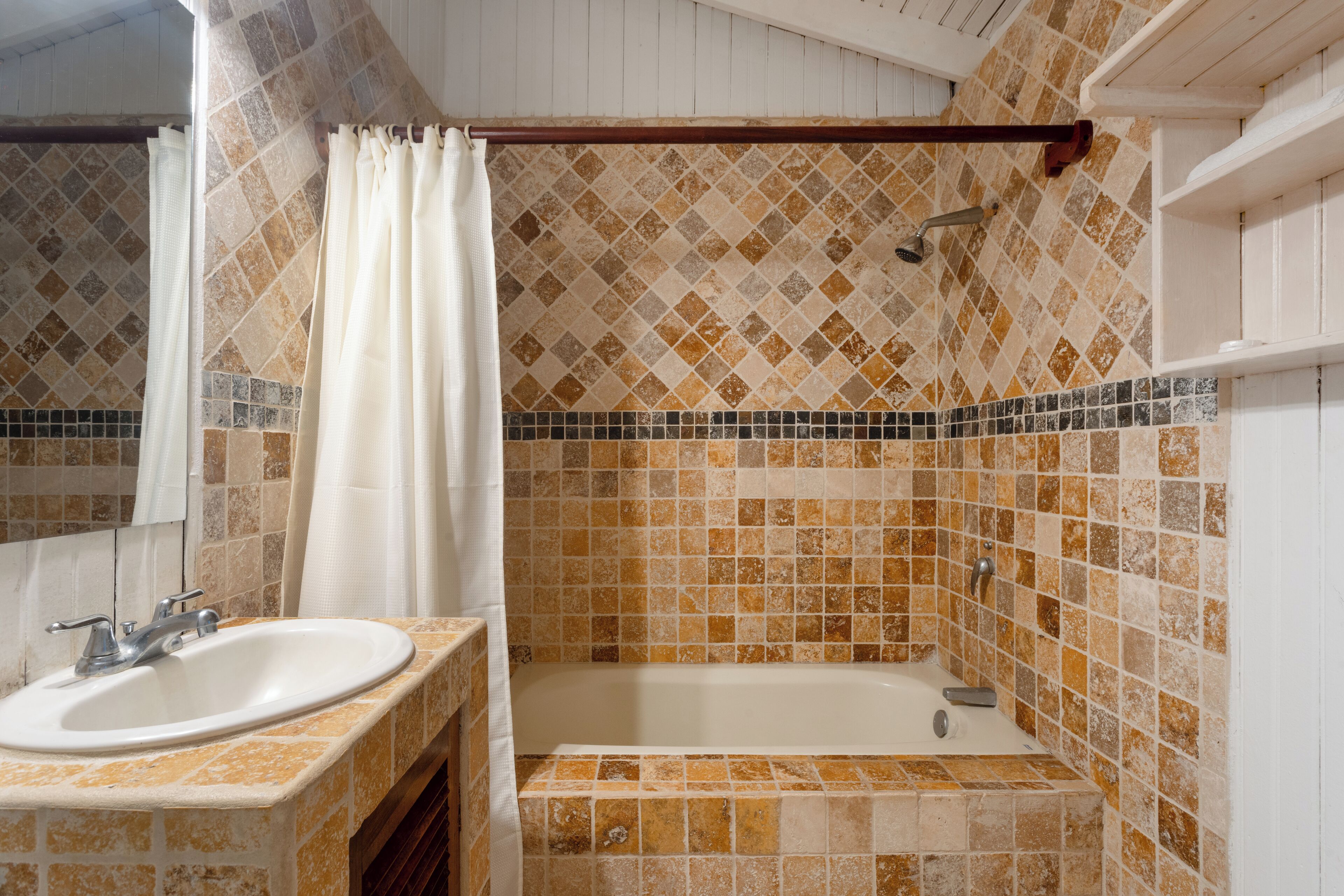 A bathroom with a sink, mirror, shower, and tiled walls.
