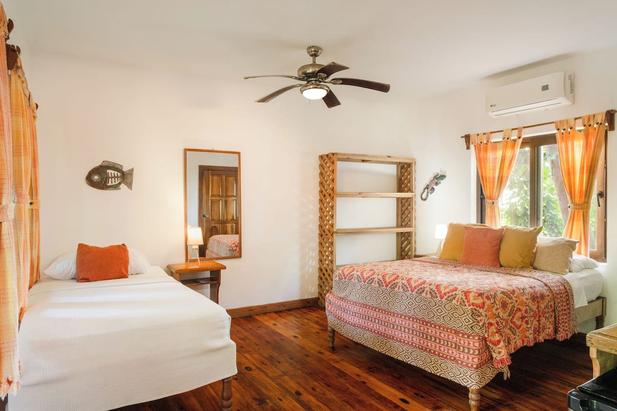 A bedroom with two beds, a ceiling fan, an air conditioning unit, and a window with curtains.