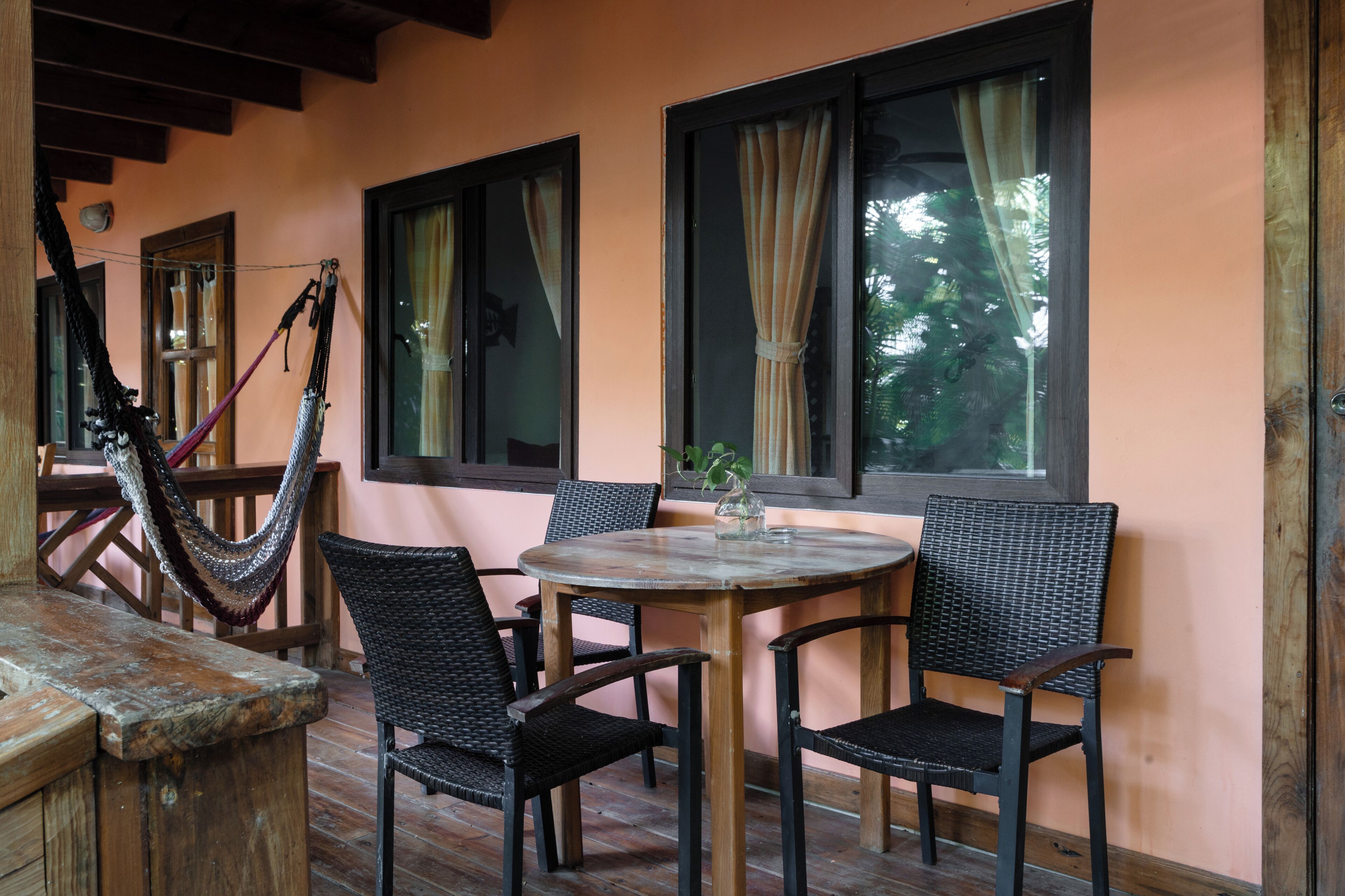 A wooden table with four wicker chairs, a hammock, and a window with curtains.