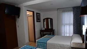 Una habitación de hotel con dos camas, un televisor, un escritorio y un espejo.