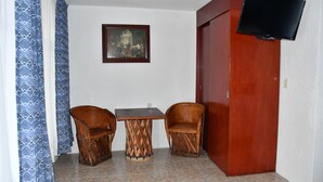 Una habitación con puerta de madera, televisor en la pared, una mesita y dos sillas.