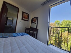 A bedroom with a bed, a desk, a mirror, and a balcony with a view of trees. - Hotel Posada Santa Fe (Zapopan)