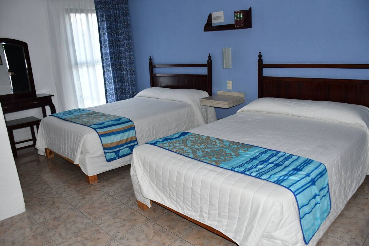 A hotel room with two beds, a desk, and a mirror.