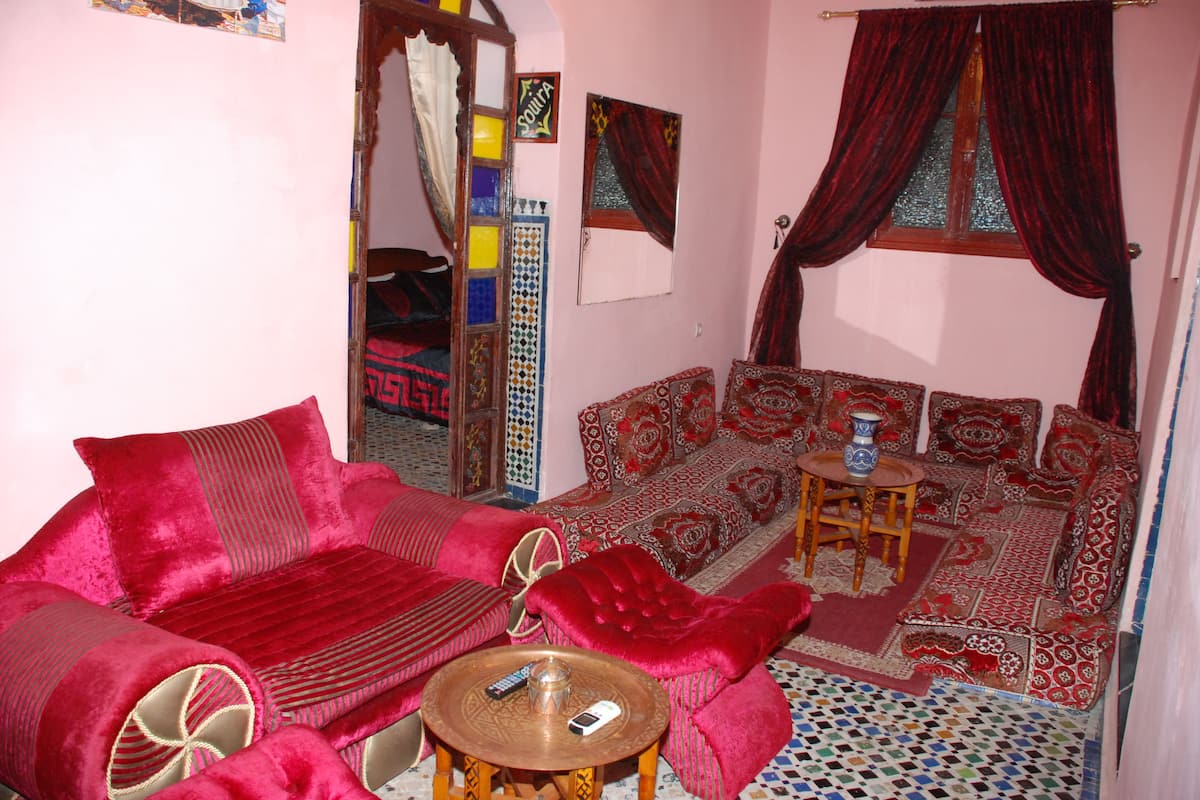 A cozy living room with a red sofa, patterned cushions, a small wooden table, and a tiled floor.