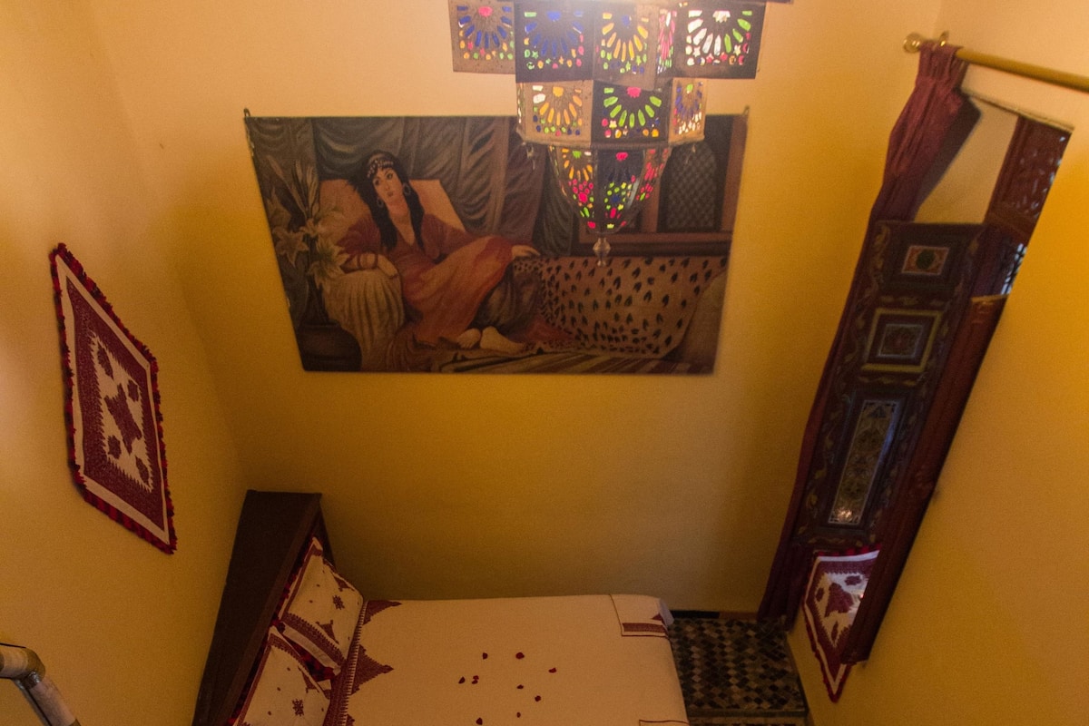 A room with a bed, a small table with a decorative item, a wall hanging, and a patterned rug.